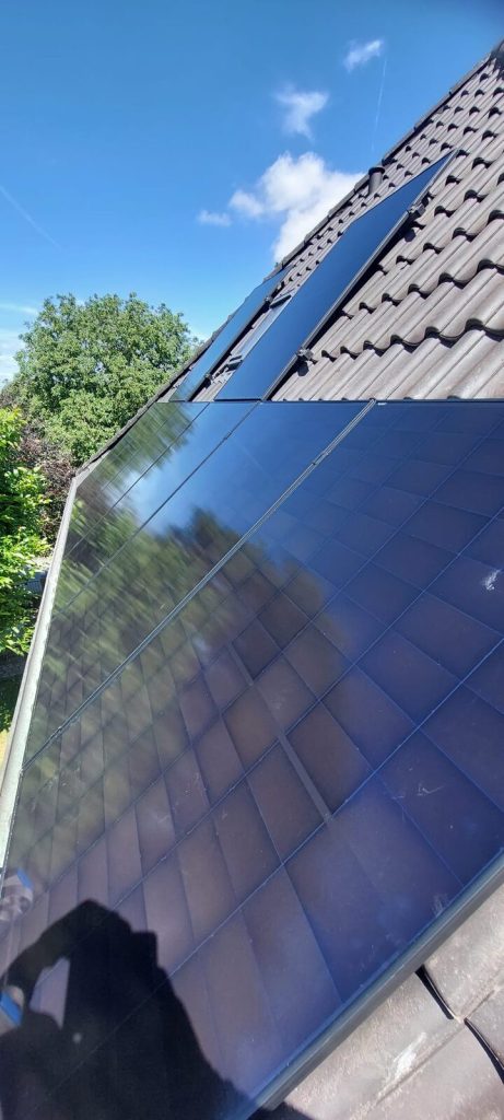 Montierte Full-Black-Solarmodule auf einem Ziegeldach vor blauem Himmel
